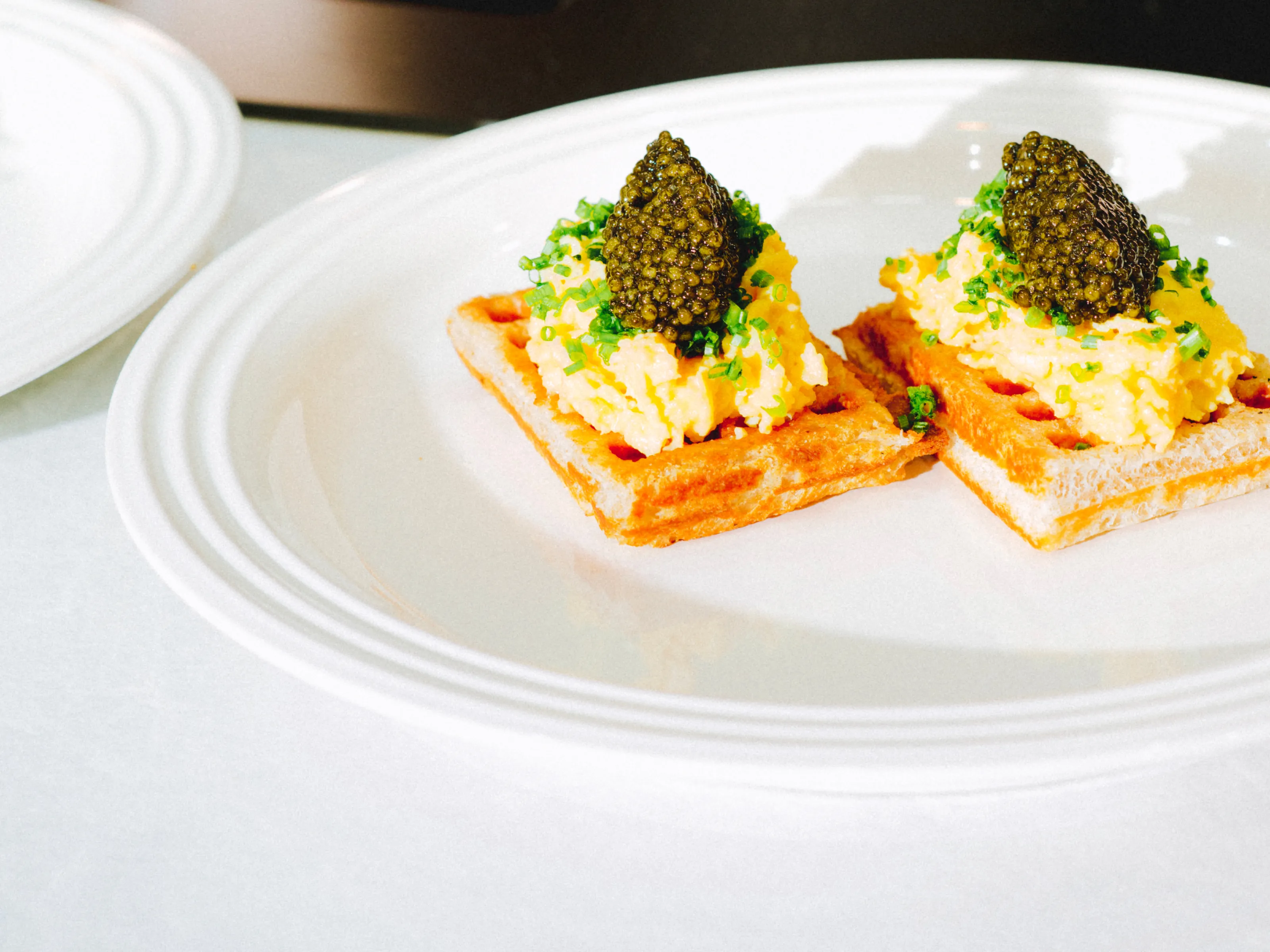 Two waffles topped with scrambled eggs, caviar, and herbs on a white plate.