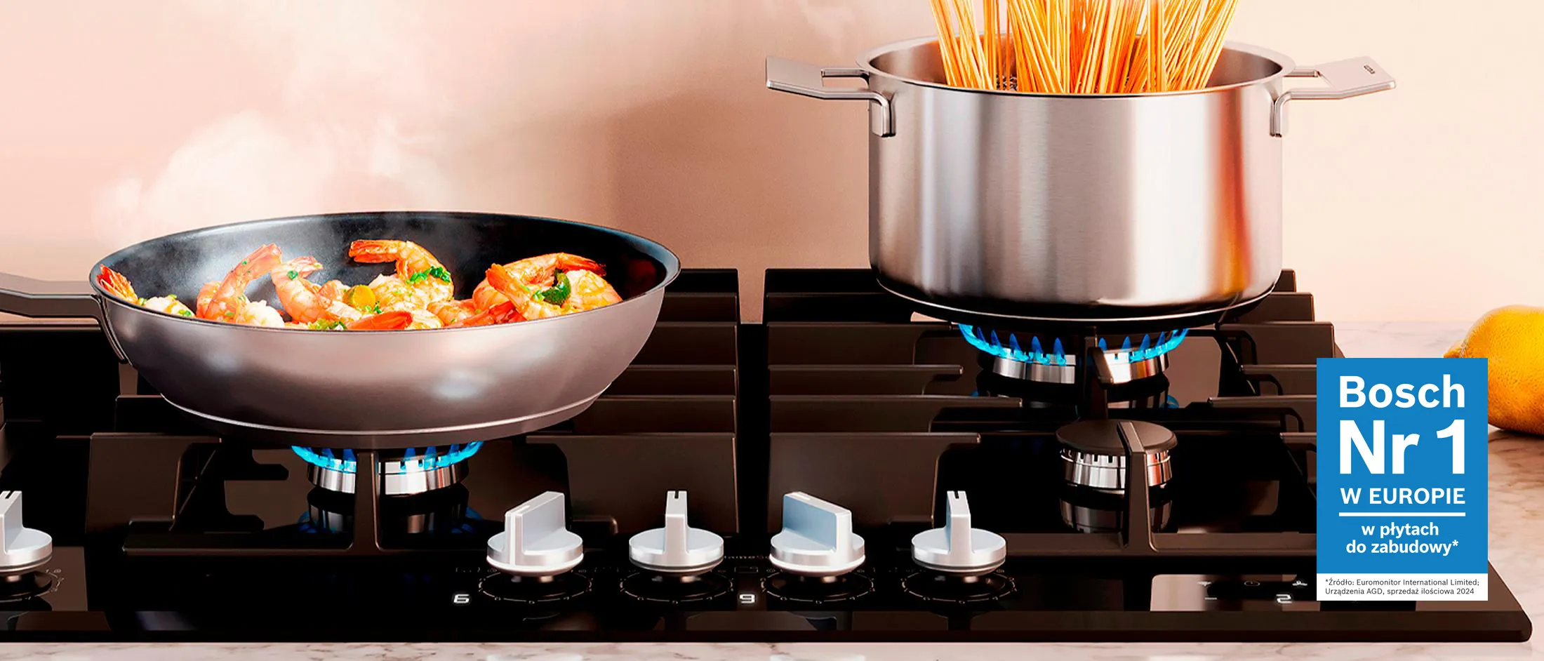 Płyta grzewcza z patelnią pełną kolorowych warzyw i garnkiem z gotującym się spaghetti, obok świeżych cytryn.