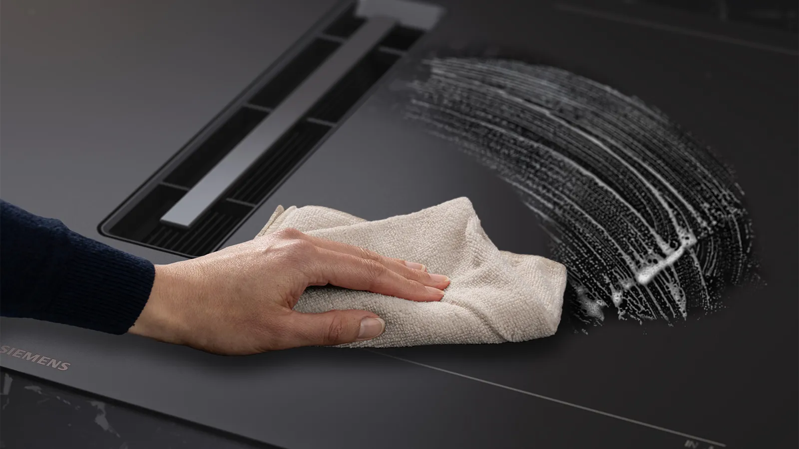 Person cleaning matt black hob surface