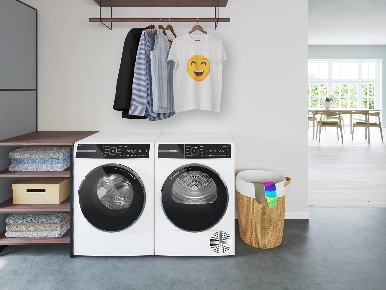 A modern laundry area features a stacked washer and dryer, neatly folded towels, a clothing rack with a smiley t-shirt, and a woven hamper.