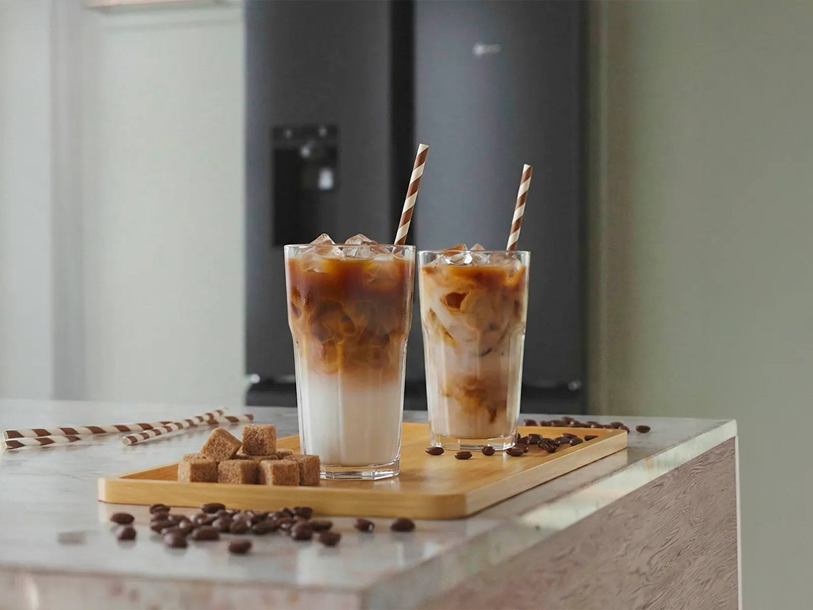Two iced coffee drinks with milk and ice on a kitchen counter, with a NEFF MultiDoor refrigerator in the background.