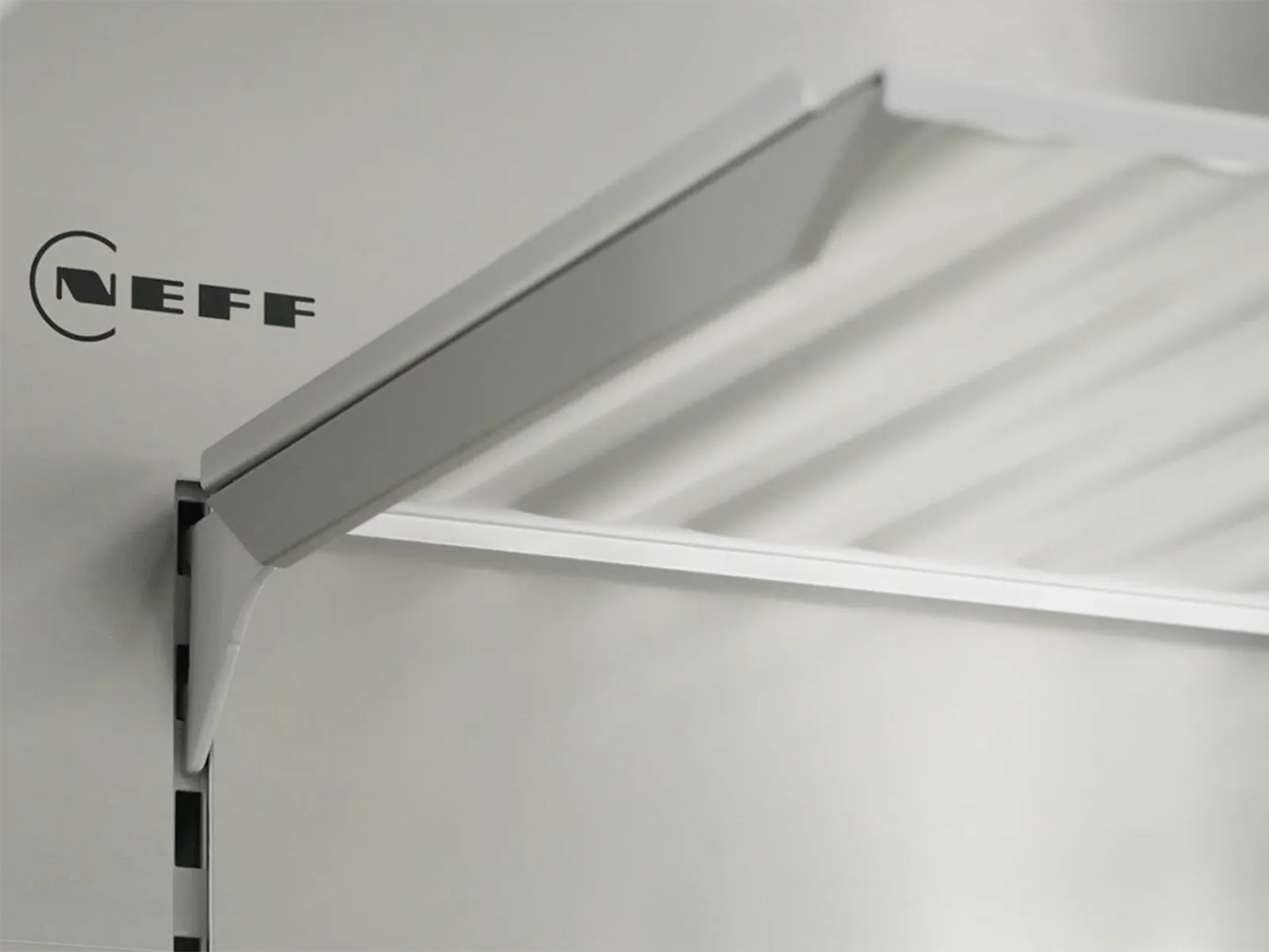 Close-up of a refrigerator’s metal back wall and glass shelf with NEFF logo.
