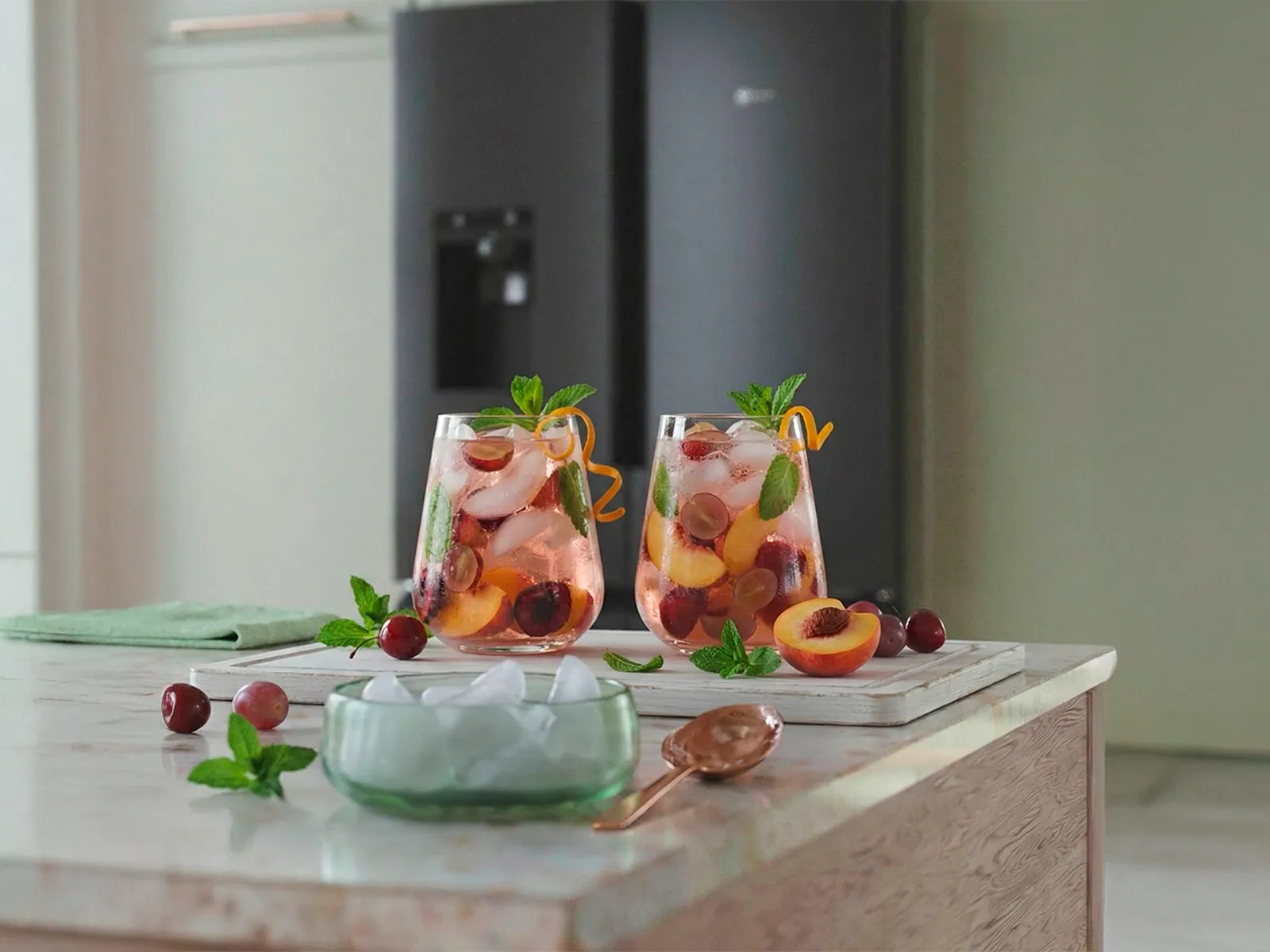 Two glasses of fruit-infused iced drinks on a kitchen counter, with a NEFF MultiDoor refrigerator in the background.