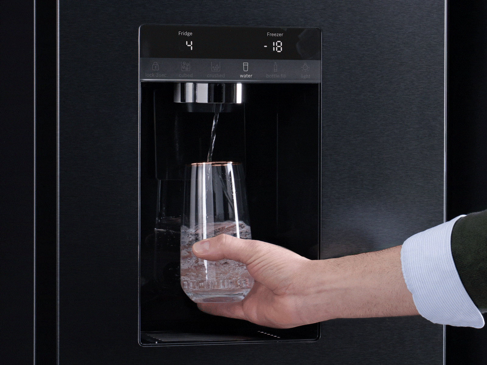Hand holding a glass as water pours from a NEFF MultiDoor Ice Water Dispense