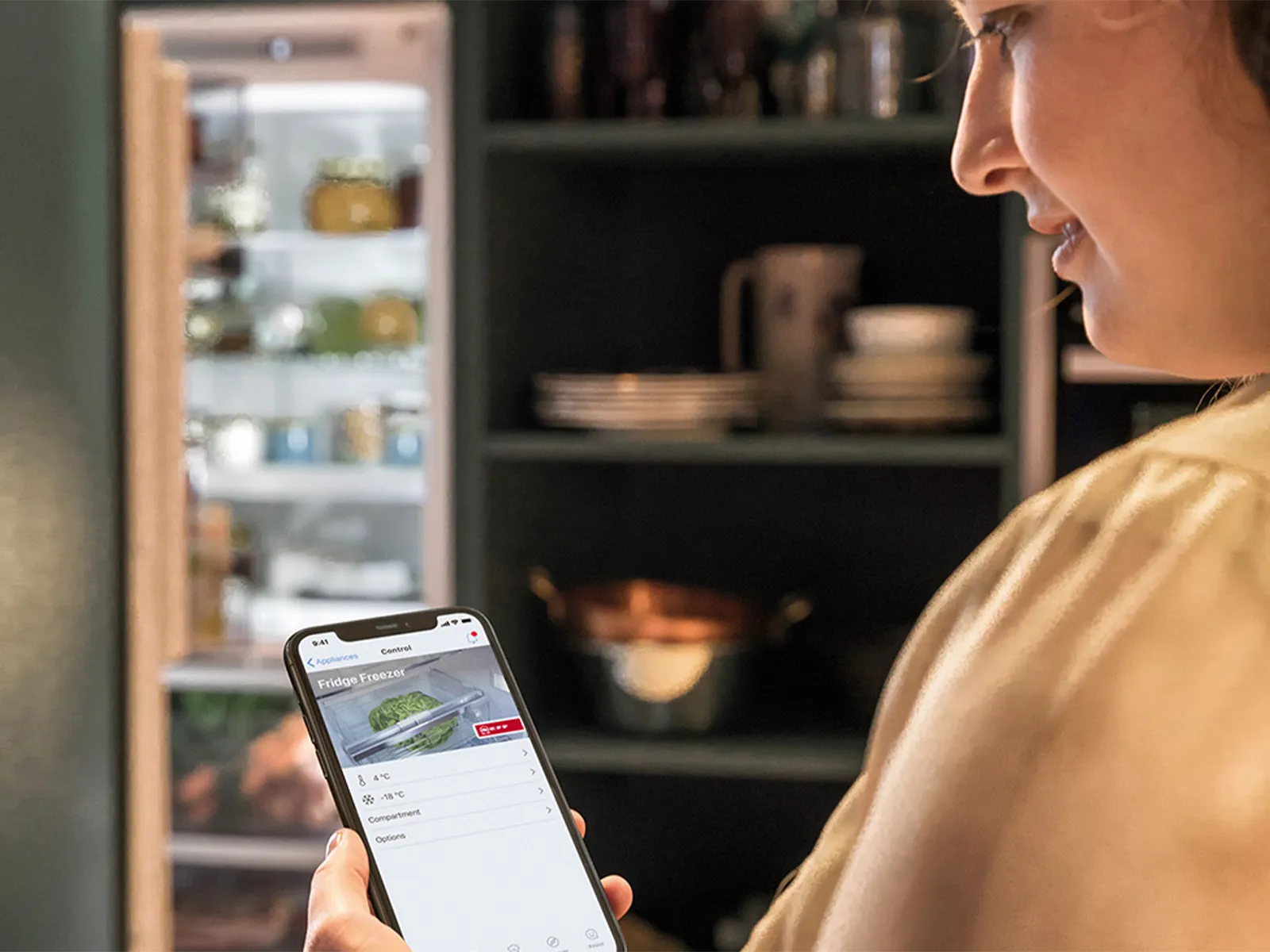 Person using a smartphone app to control a refrigerator, with the open fridge in the background.