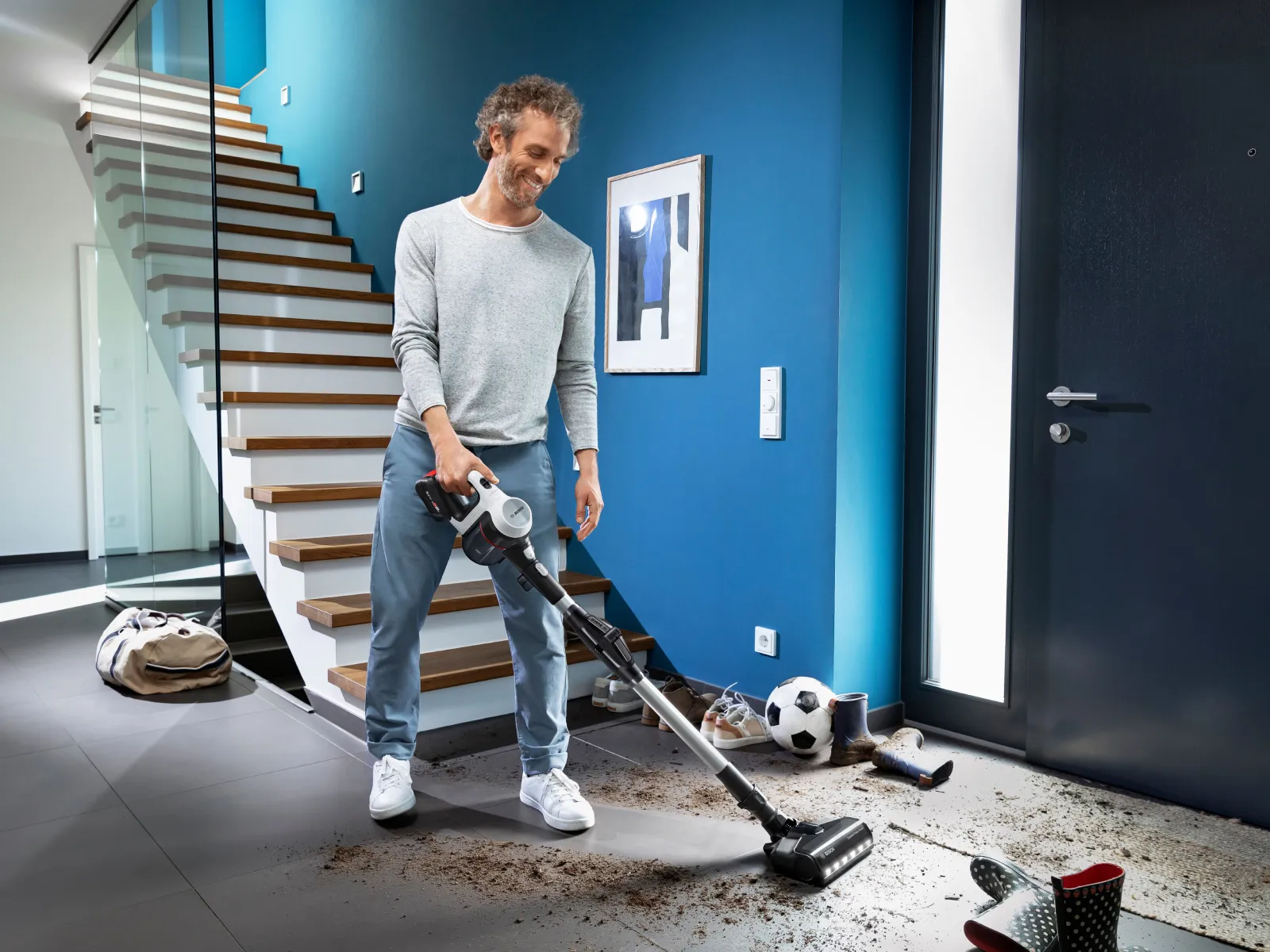 Man using vacuum cleaner in home with soccer ball and "Intelligent Power" text overlay.