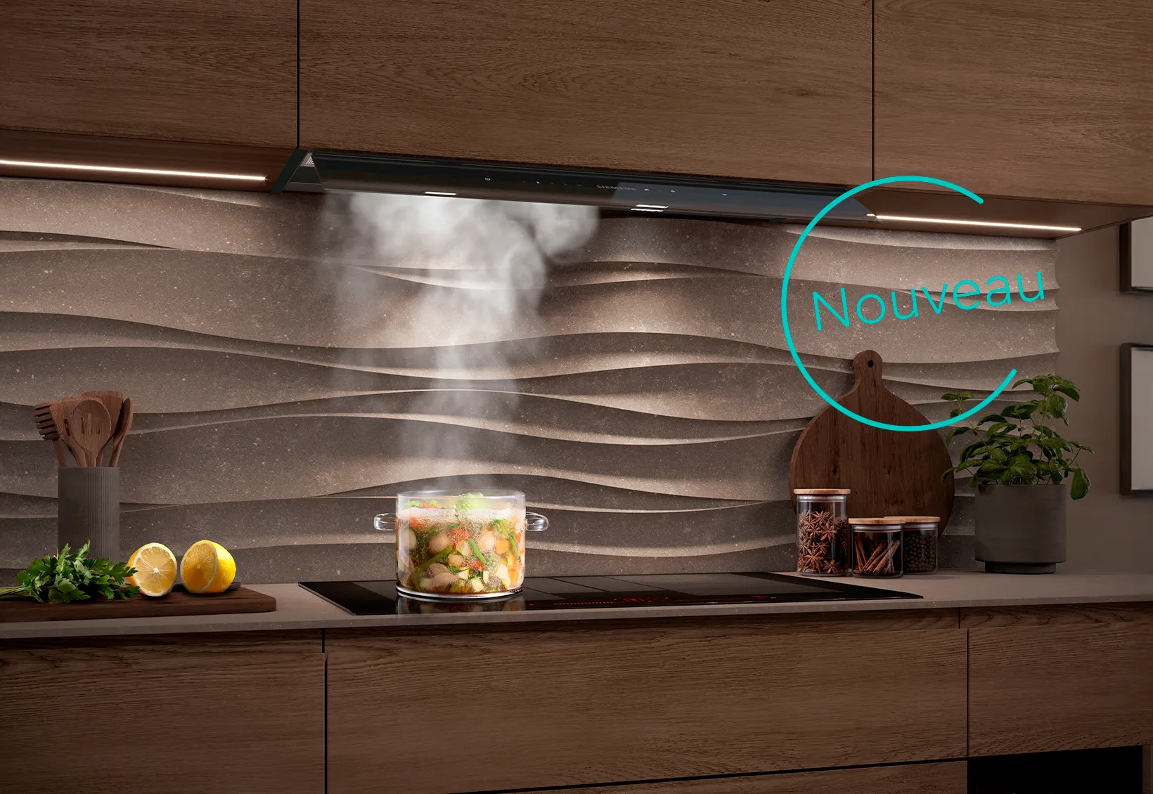 Cuisine moderne avec une casserole en verre de légumes fumants sur une plaque de cuisson à induction. Au-dessus, une hotte aspirante intégrée et éclairée devant une crédence texturée et ondulée.