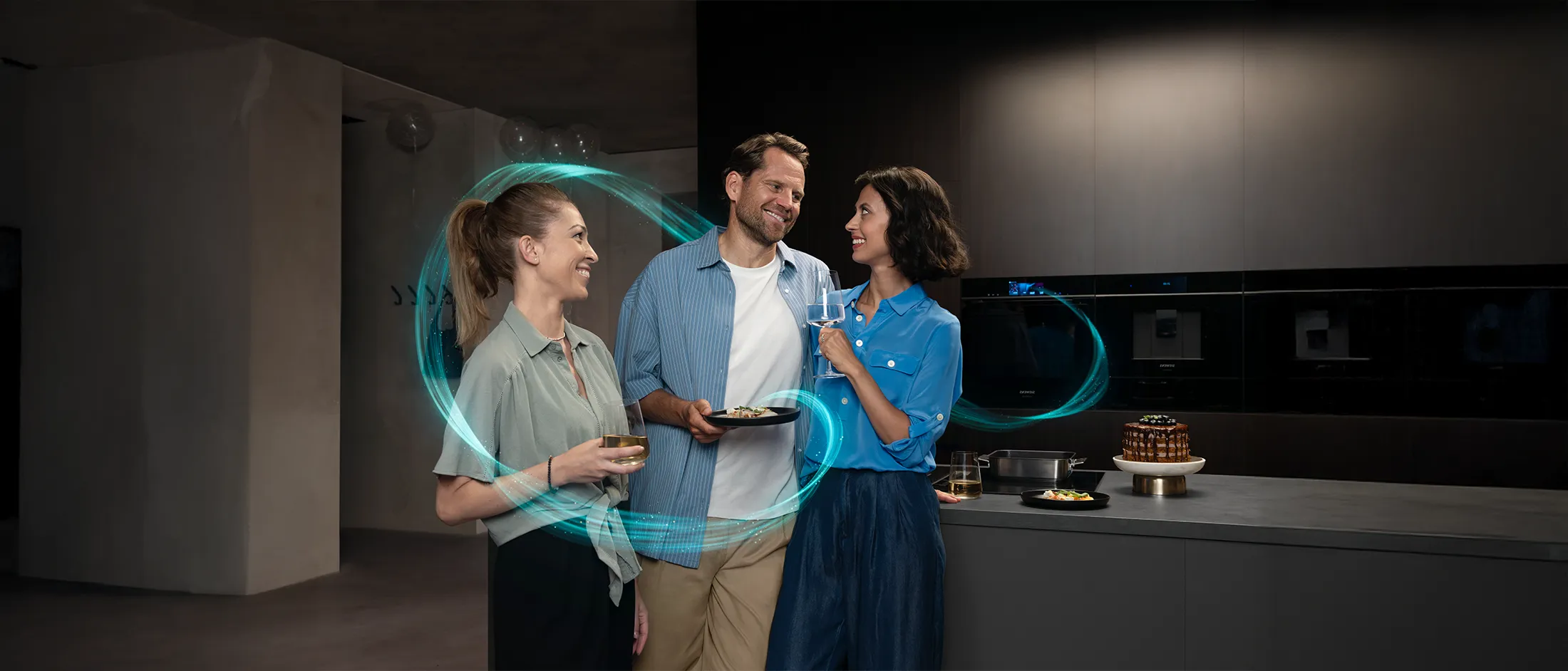 Tres personas disfrutan de bebidas y aperitivos en una cocina moderna, rodeada de una luz suave y un diseño elegante.