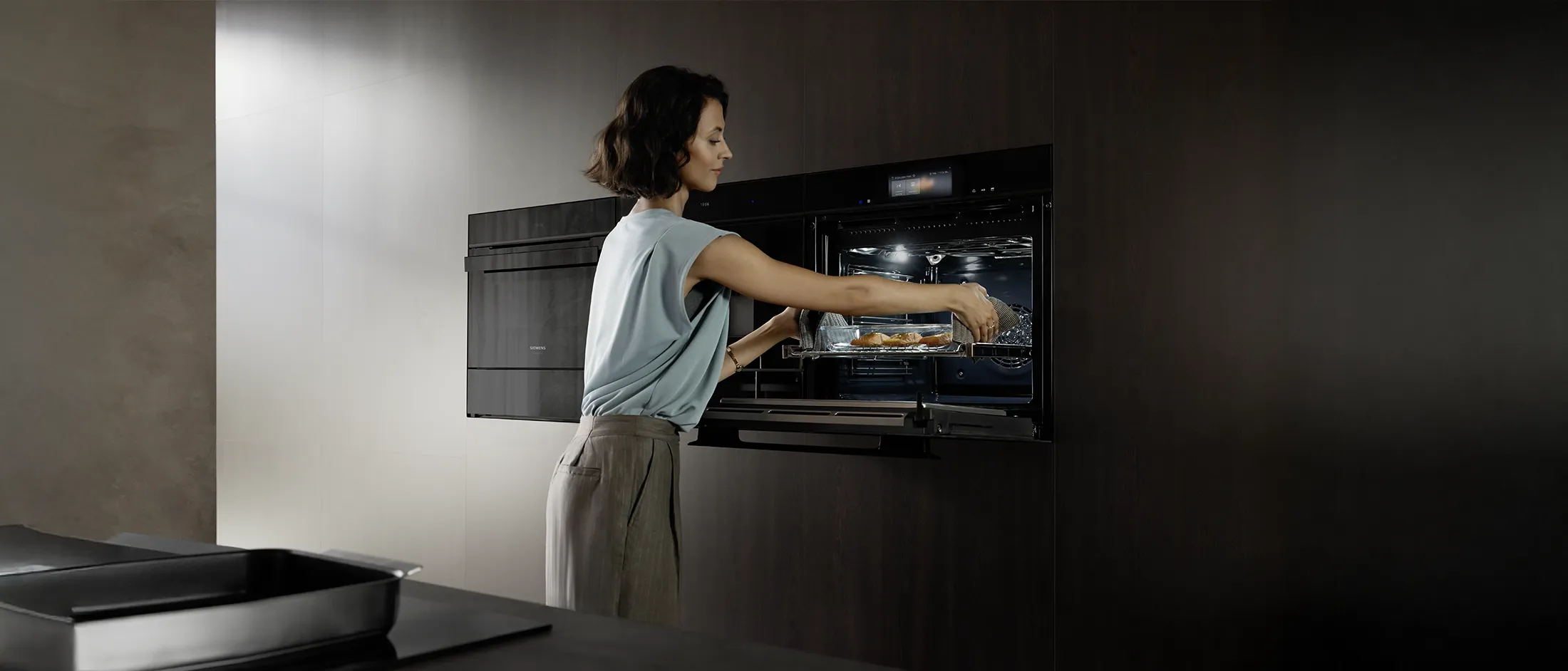  Una joven introduce una bandeja con alimentos en su horno con cámara integrada e inteligencia artificial