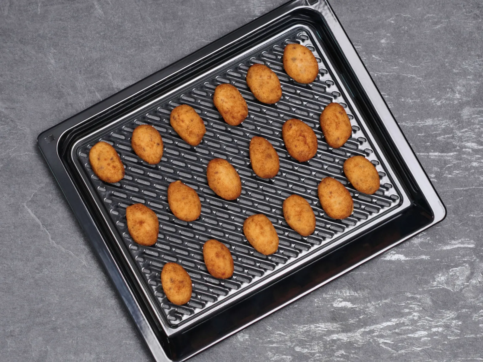 Horno compacto con función air fryer visto desde arriba: bandeja de rejilla con varias croquetas doradas alineadas, sobre una encimera gris.
