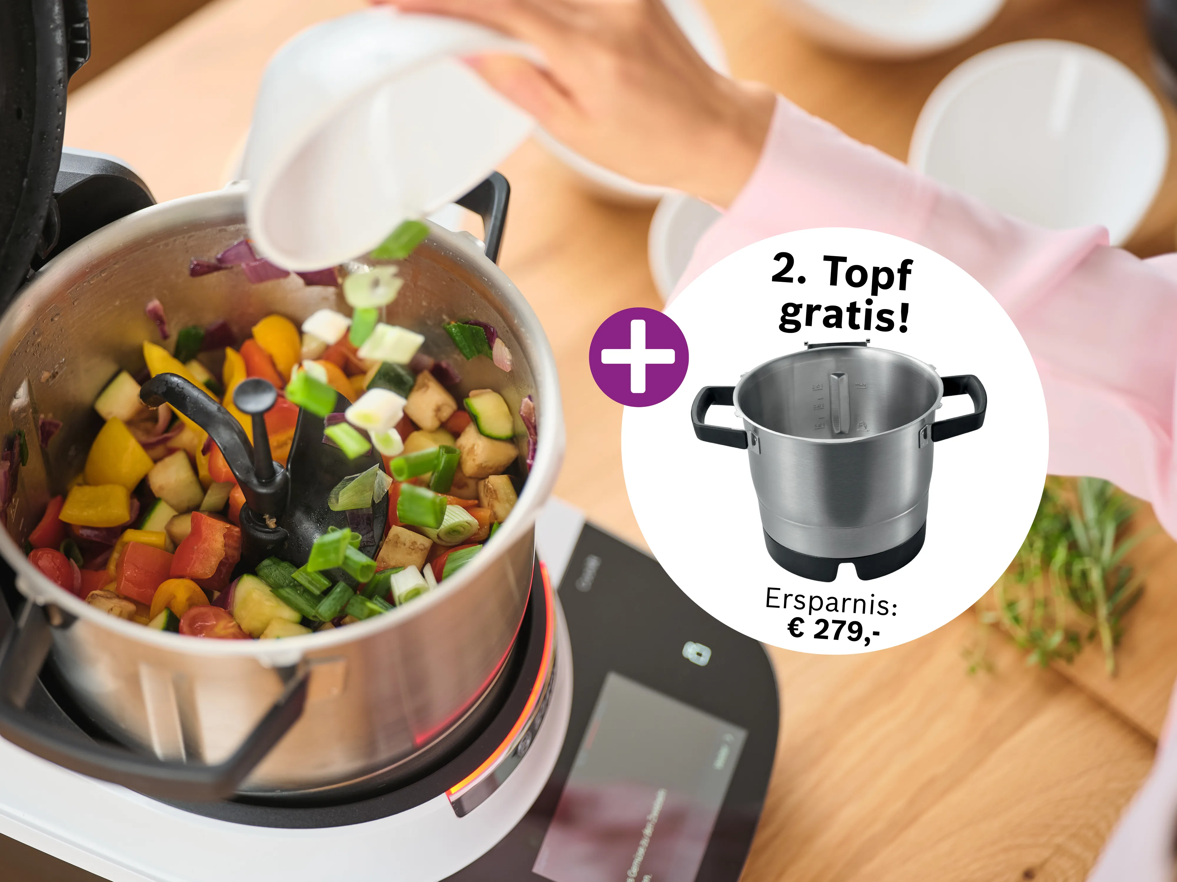 Eine Person füllt Gemüse in eine Cookit Küchenmaschine. Daneben wird ein zweiter Topf als Gratis-Zugabe beworben, mit einem Ersparnis von 279 Euro.