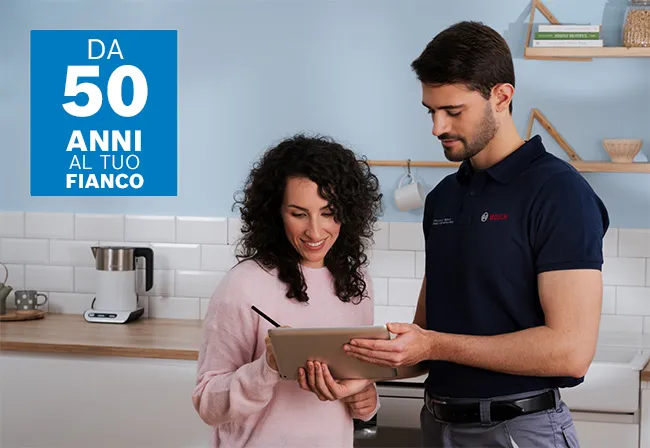 L'immagine mostra un interno cucina con un uomo che ripara una lavastoviglie, circondato da moderni armadi bianchi e elettrodomestici.