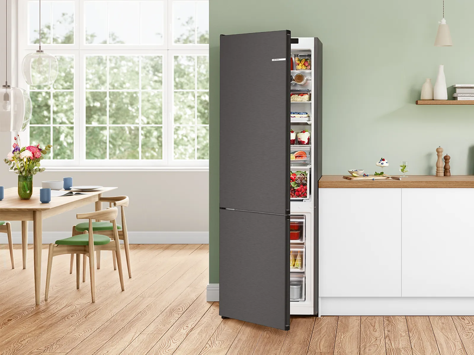 Ein moderner grauer Kühlschrank mit Gefrierfach unten steht an einer hellgrünen Wand in einer hellen Küche mit Holzboden.