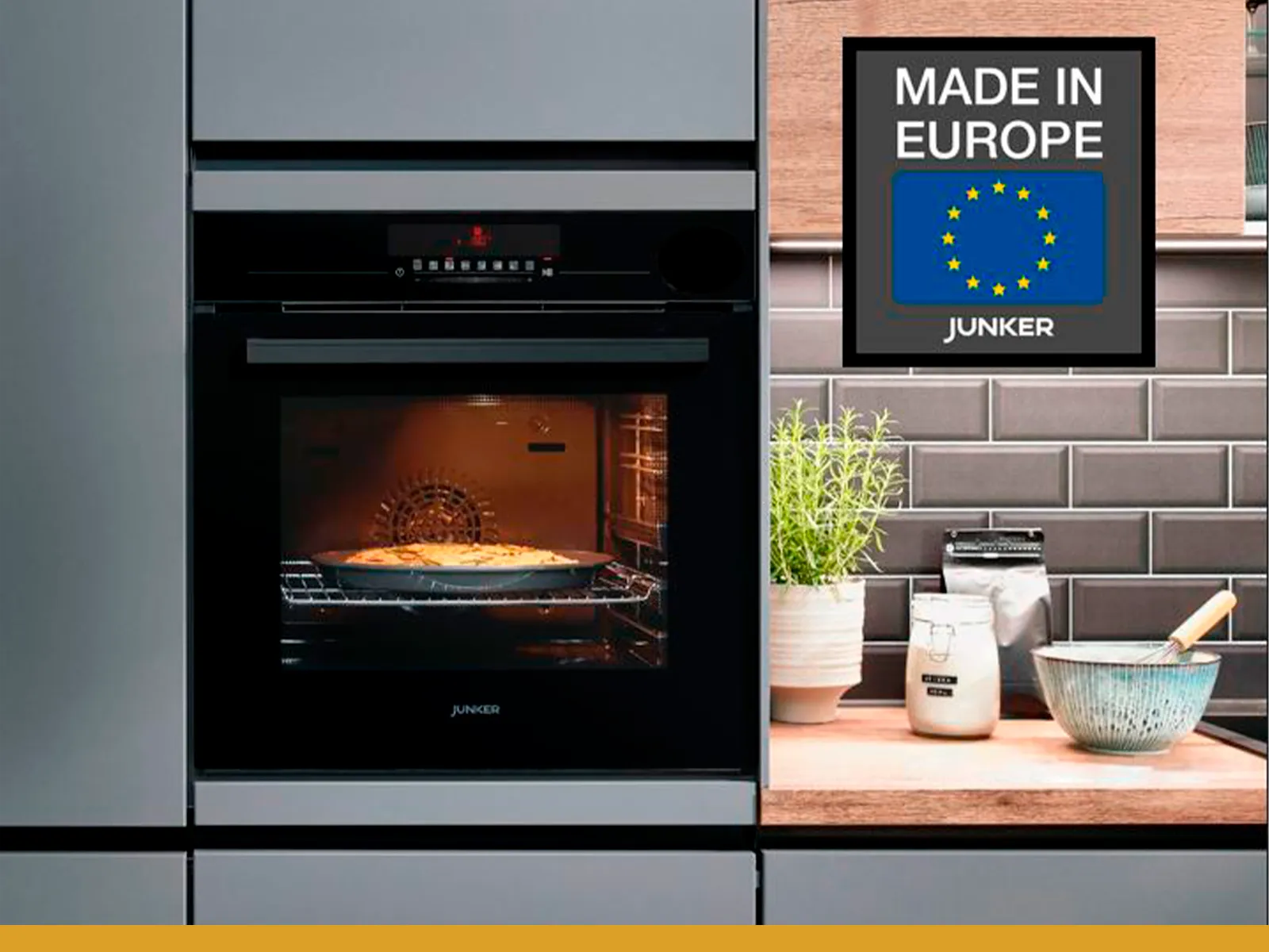 Moderne Küche mit schwarzem Ofen, „Made in Europe“-Schild, Pflanzen und Kochgeschirr auf der Arbeitsplatte.