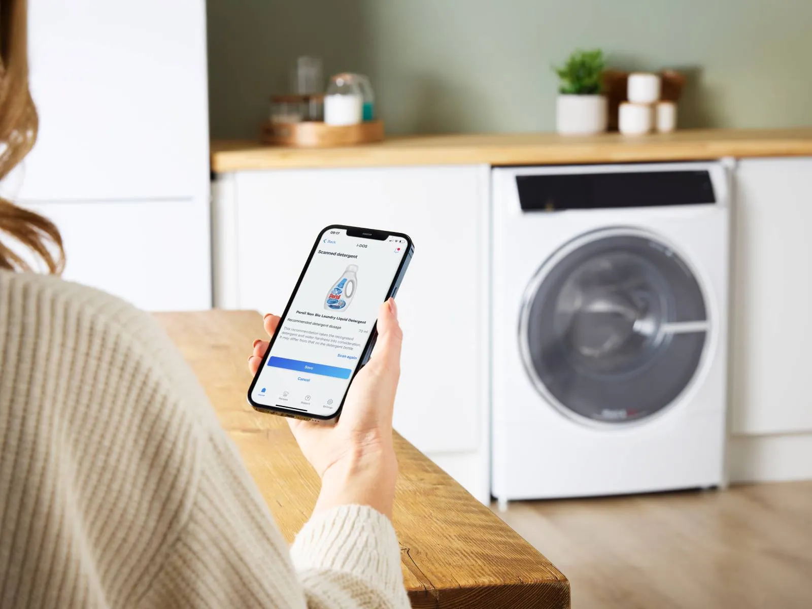A person using a smartphone app to manage detergent settings for a washing machine in a modern laundry area.