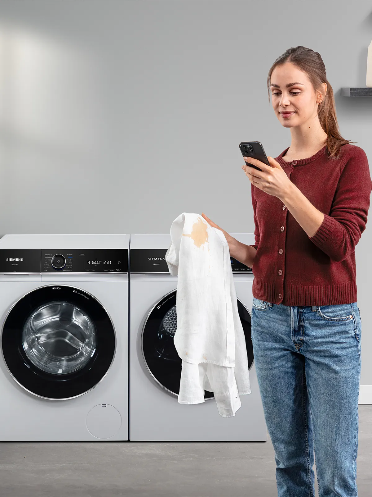 woman checking the Home connect app for stain removal programme holding a white shirt