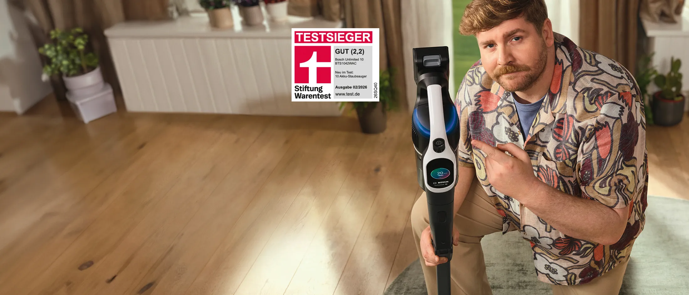 Ein blonder Mann mit Bart und buntem Hemd präsentiert den Akku-Staubsauger Testsieger Unlimited 10 von Bosch.