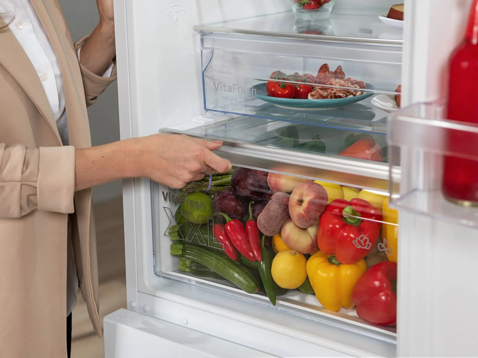 A view inside a refrigerator showcasing fresh fruits and vegetables in organized drawers, along with fish on a plate above.