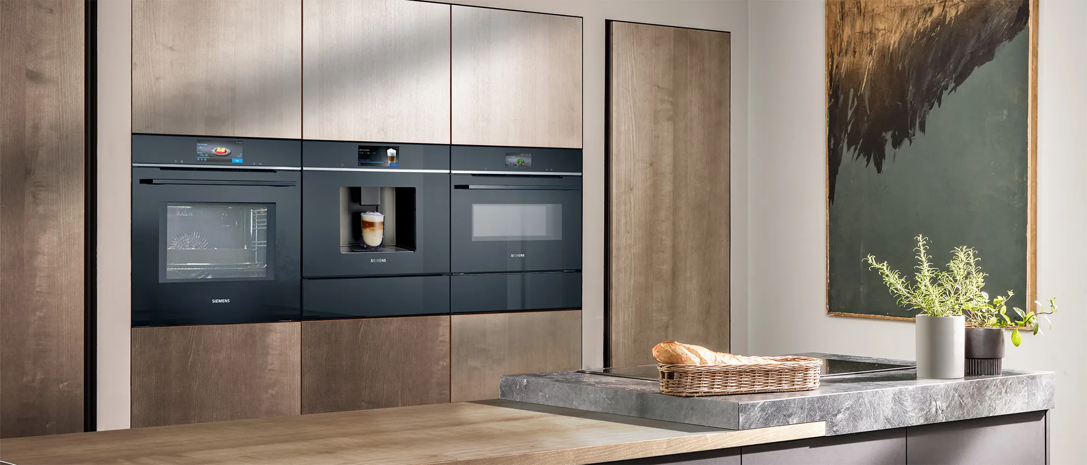 Modern kitchen featuring sleek built-in black appliances, a stone countertop, and decorative elements like a painting and a bread basket.