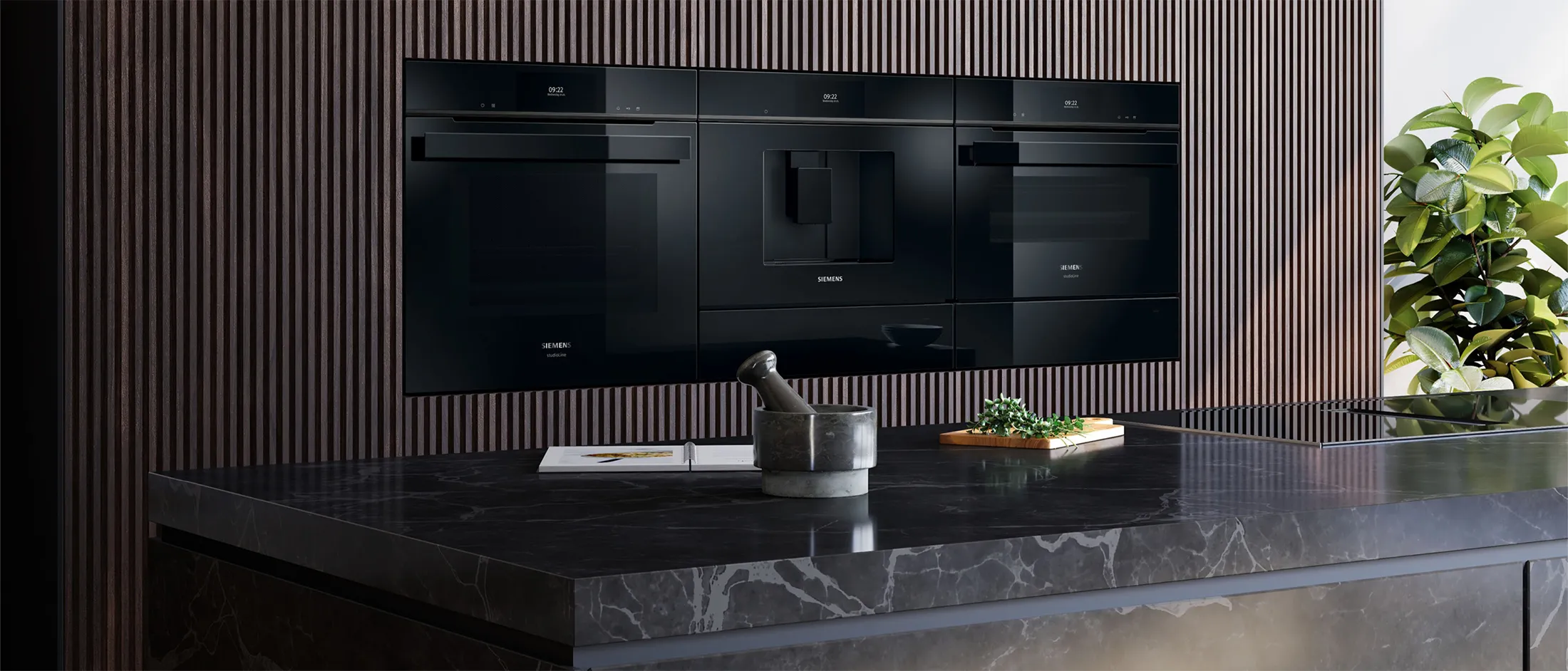 Modern kitchen featuring sleek black appliances, a dark marble countertop, and a textured wood accent wall with greenery.