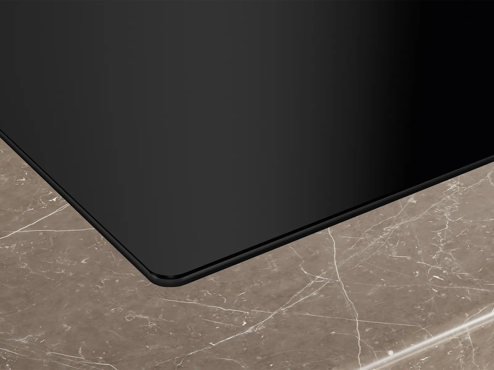 A close-up of the sleek black glass surface of a Siemens induction cooktop, seamlessly integrated into a dark marble-patterned countertop.