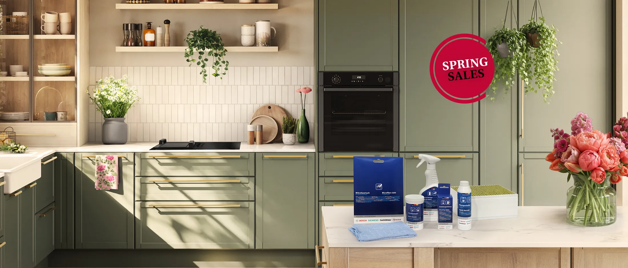 Modern kitchen with green cabinets, white countertop, cleaning products on island, hanging plants, fresh flowers, and a "Spring Sales" sign.
