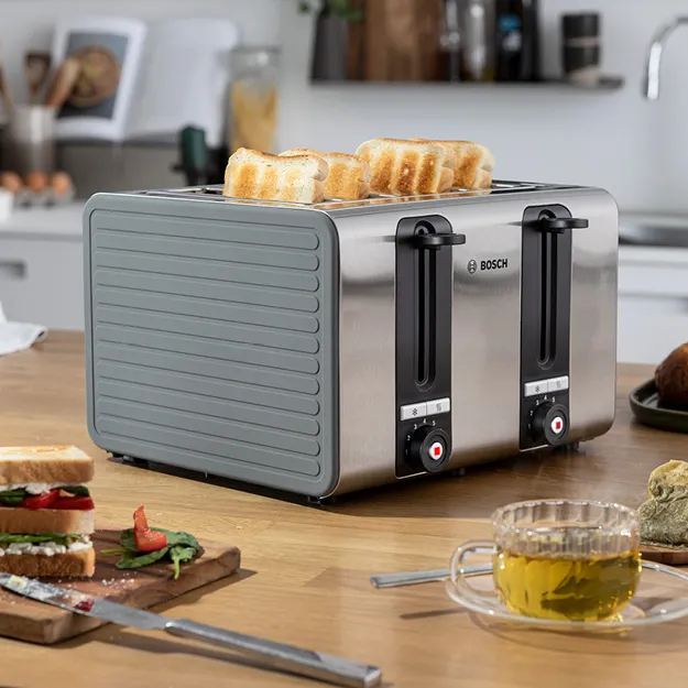 Stainless steel toaster on kitchen counter with various breakfast items, including croissants and berries.