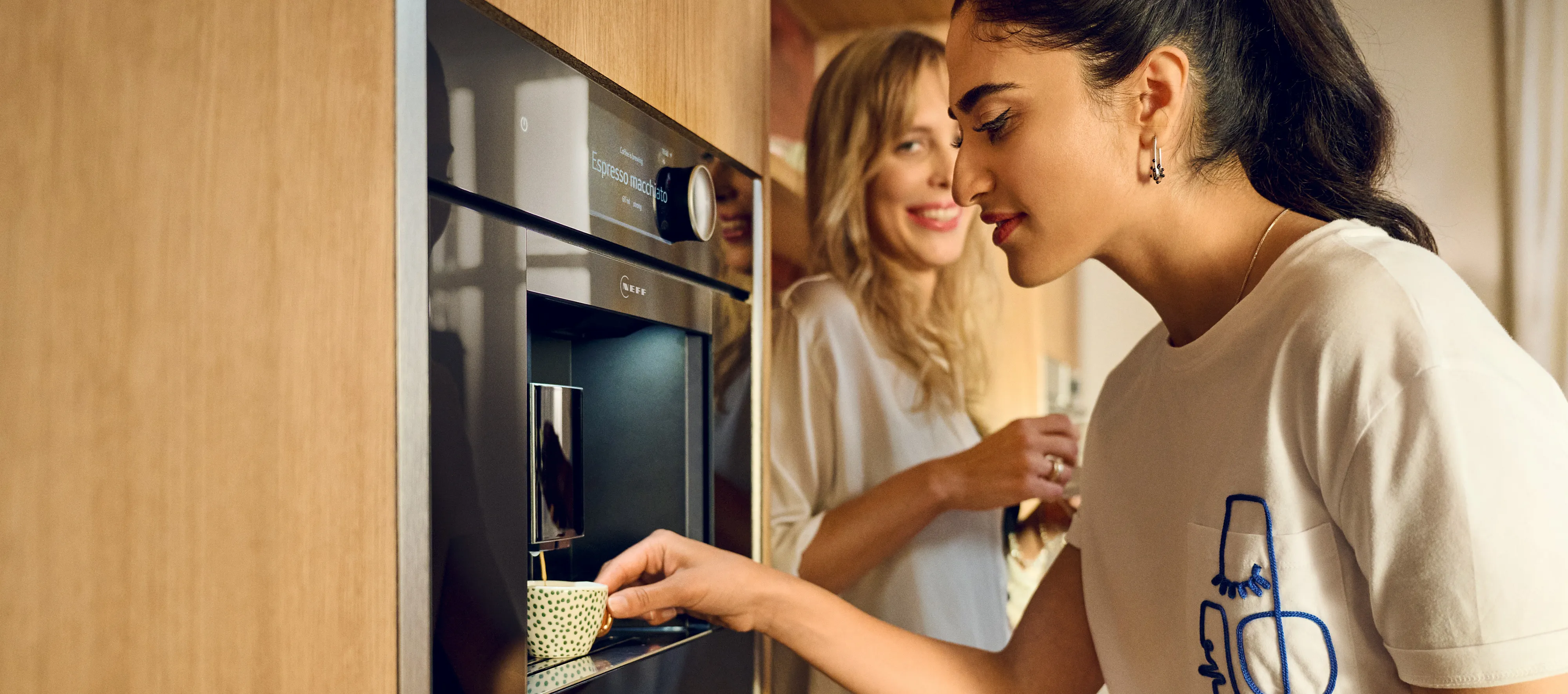 Kaks naist naudivad kohvi koos modernses köögis, kus on sisseehitatud NEFF kohvimasin.