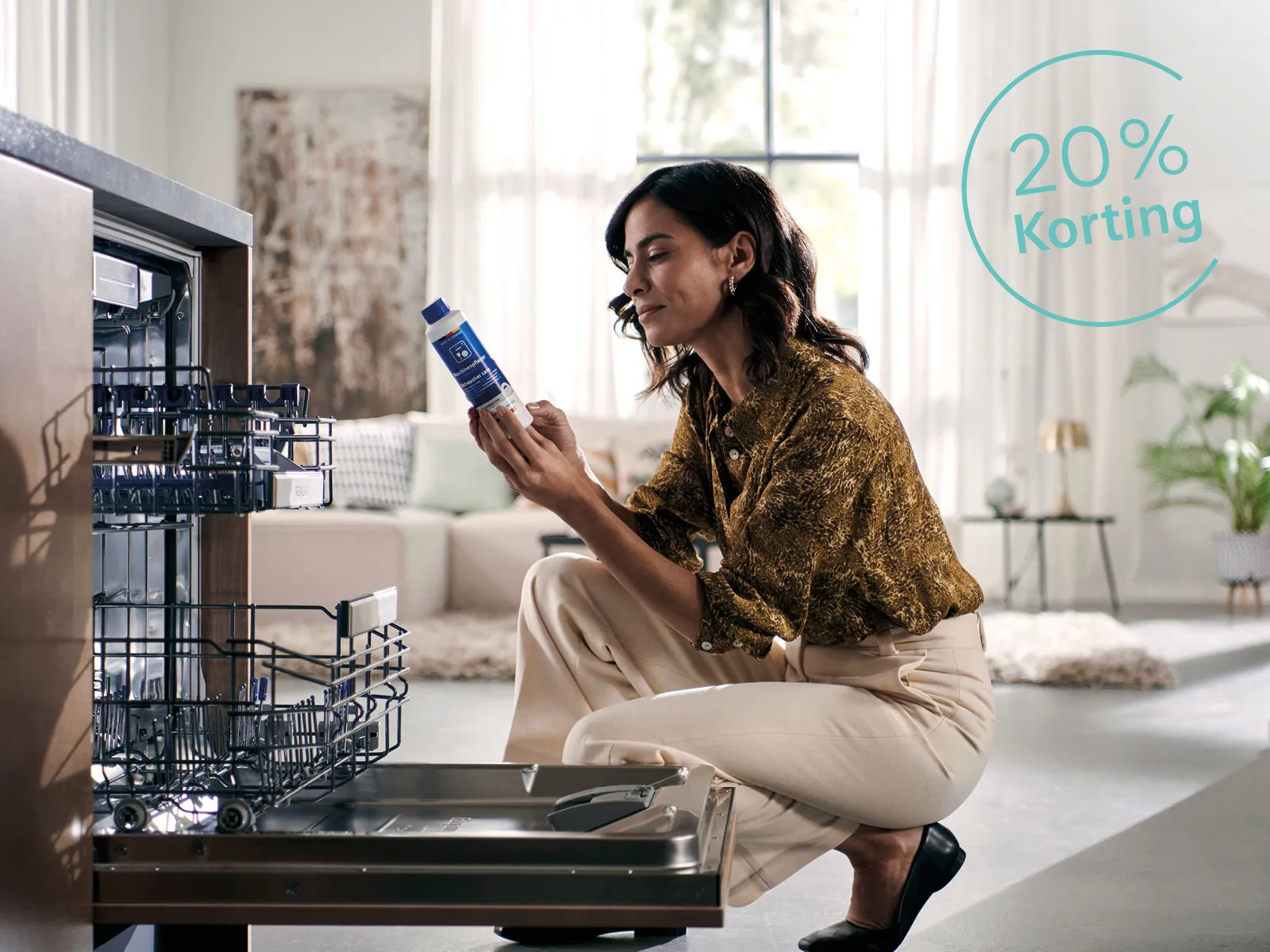 Vrouw zit voor vaatwasser met reinigingsmiddel in haar hand. 