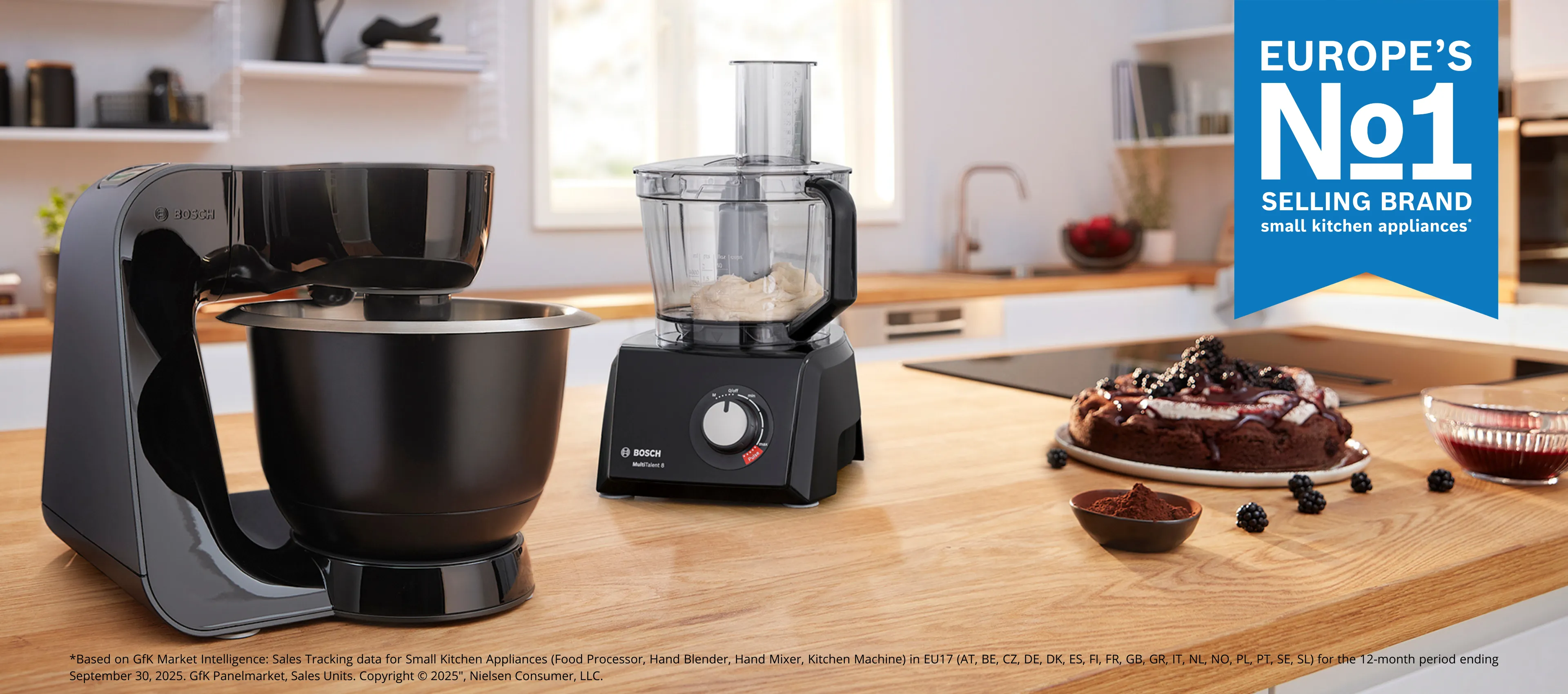 Bosch standmixers en een Bosch foodprocessor op een houten werkblad naast een cake.
