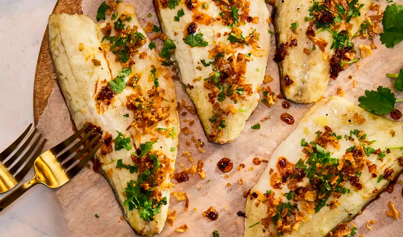 Cooked seabass on a wooden plate, served with herby shallot crumbs and coriander.
