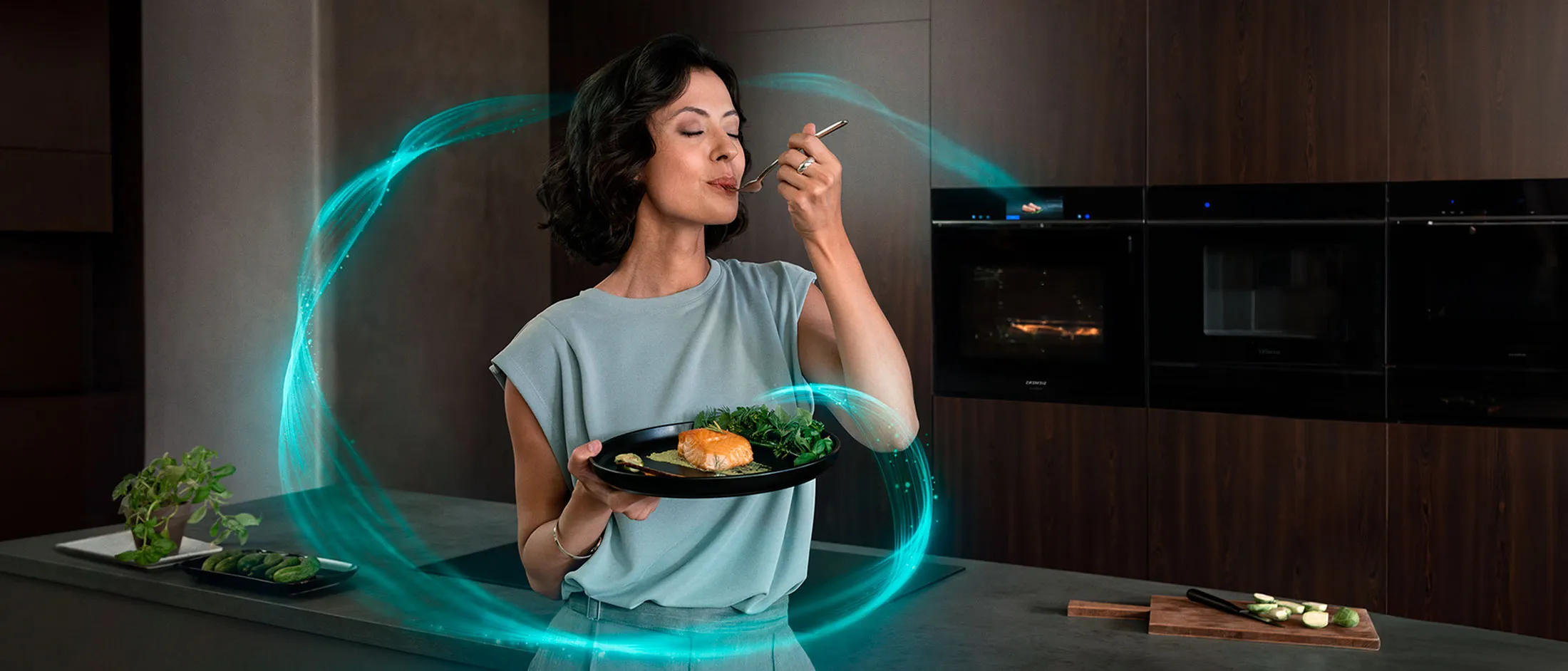 En kvinne står foran en innebygd iQ700-ovn og holder en tallerken med en lakserett og en gaffel i hånden.