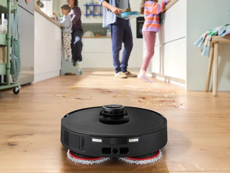 Μια ρομποτική σκούπα σε ξύλινο πάτωμα όπου καθαρίζει τις βρωμιές του πατώματος που έχει μπροστά της.