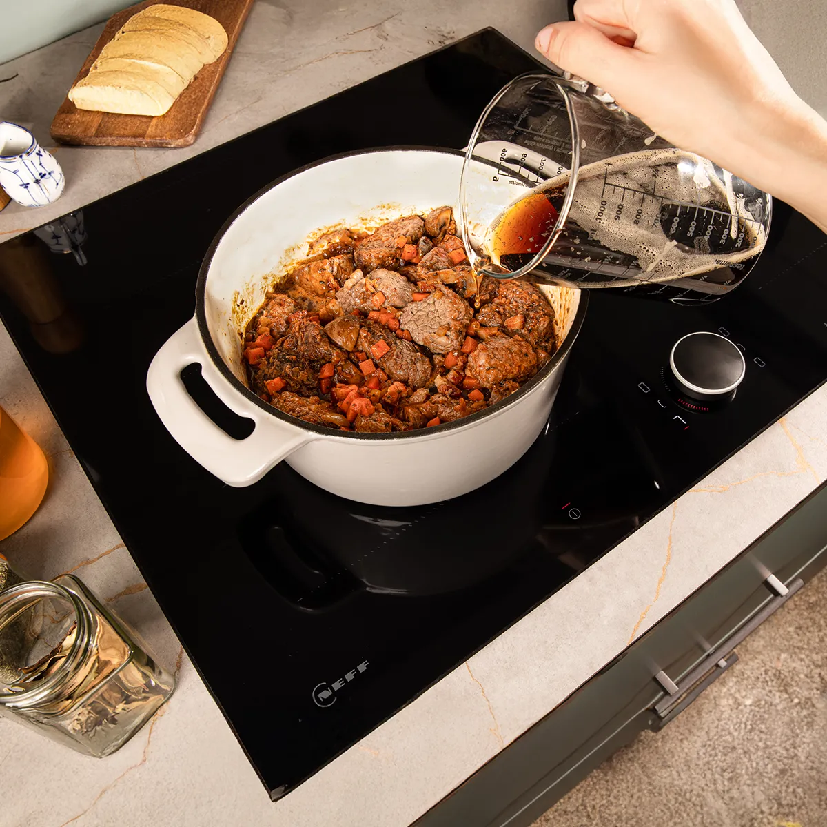 Pot of stew on electric stove, with spoon and glass jar in the background.