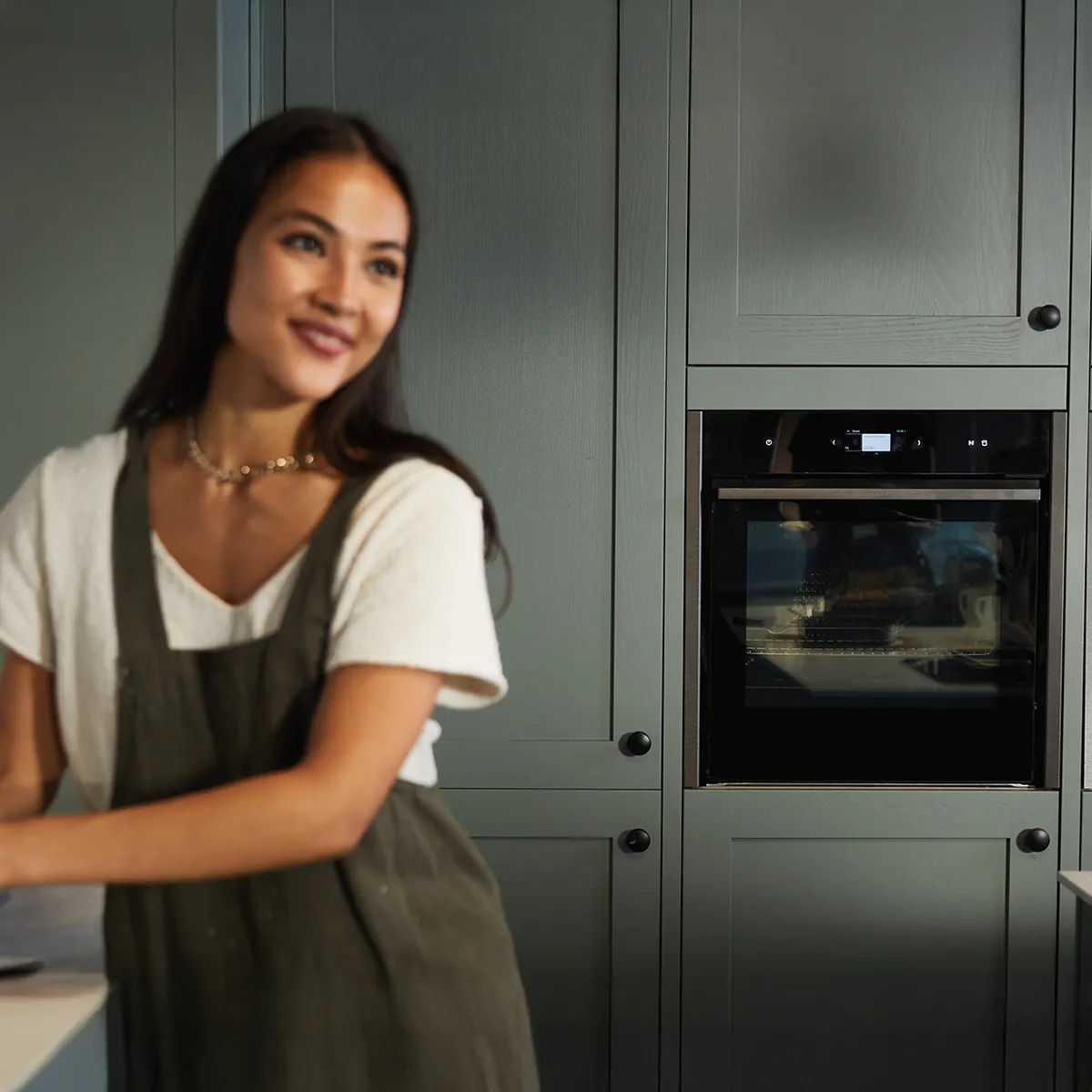 Une personne en tenue décontractée se tient près d'un comptoir de cuisine, avec des fours noirs modernes et des armoires en arrière-plan.