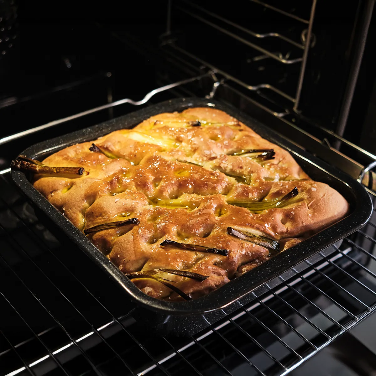 Pain focaccia doré avec des oignons verts et du sel cuisant dans un four sombre.