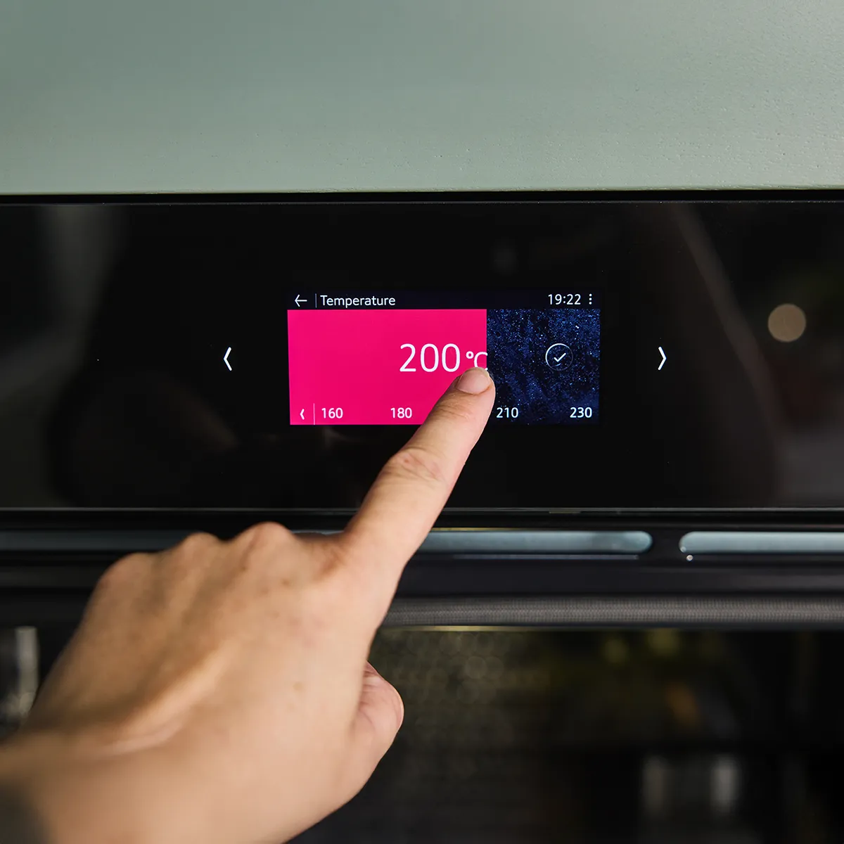 Hand setting a modern oven's digital display to 200°C.