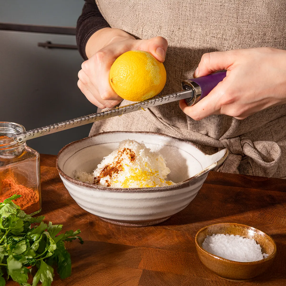 Une personne pressant un citron au-dessus d'un plat, entourée d'ingrédients de cuisine sur un plan de travail en bois.