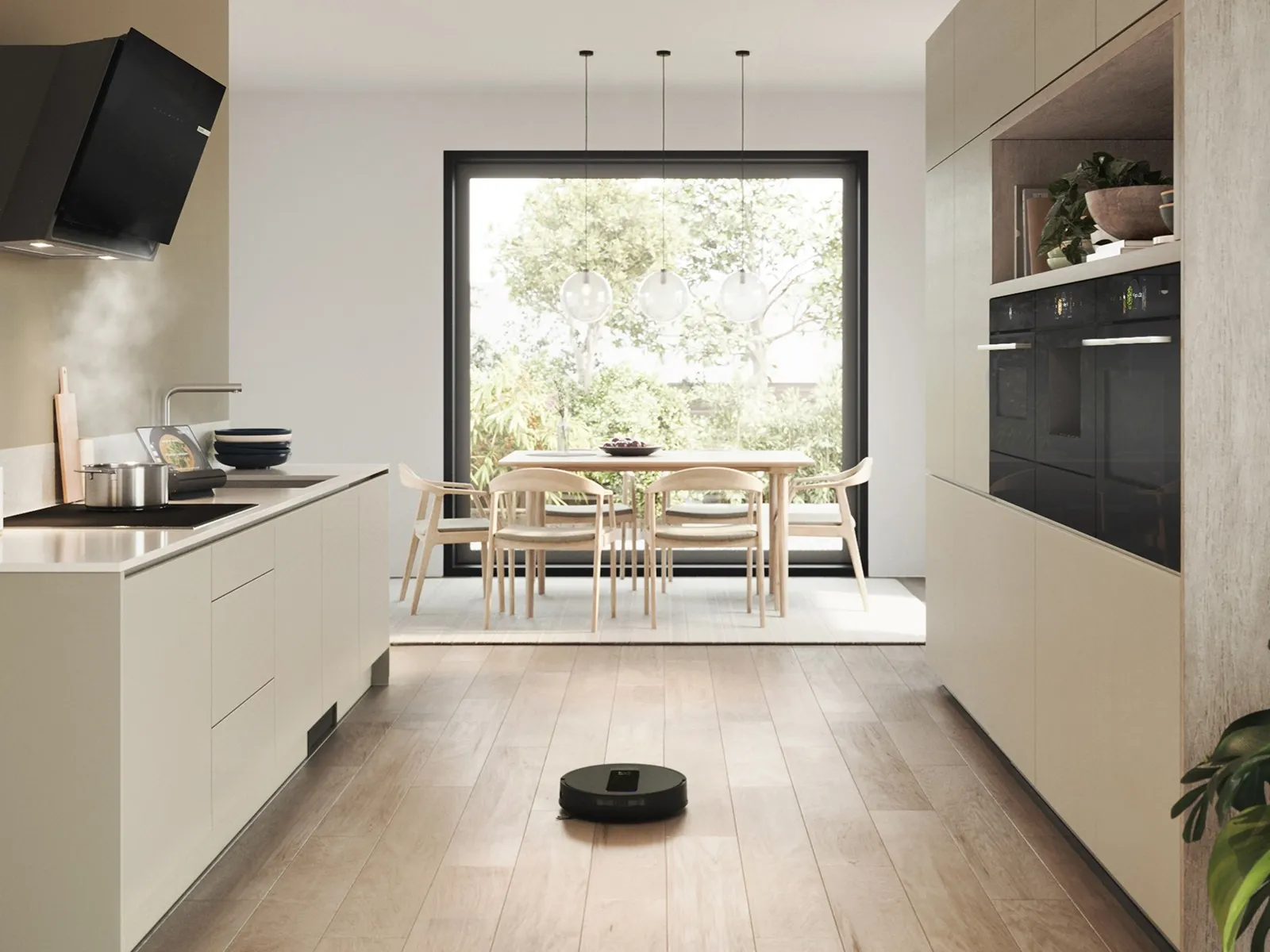 Cuisine moderne avec parquet en bois, aspirateur robot en fonctionnement, casserole fumante sur la cuisinière et coin repas près d’une grande fenêtre avec vue sur l’extérieur.