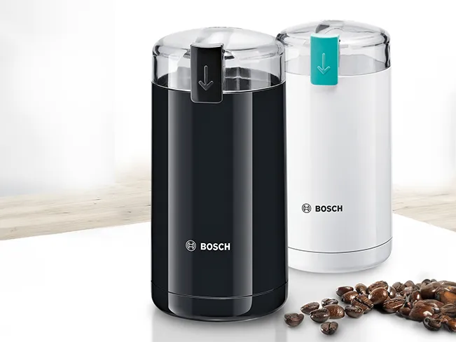 Kahve taşlamacı ve konteyner, Bosch markası, siyah ve beyaz renkler, masadaki kahve fasulyeleri.