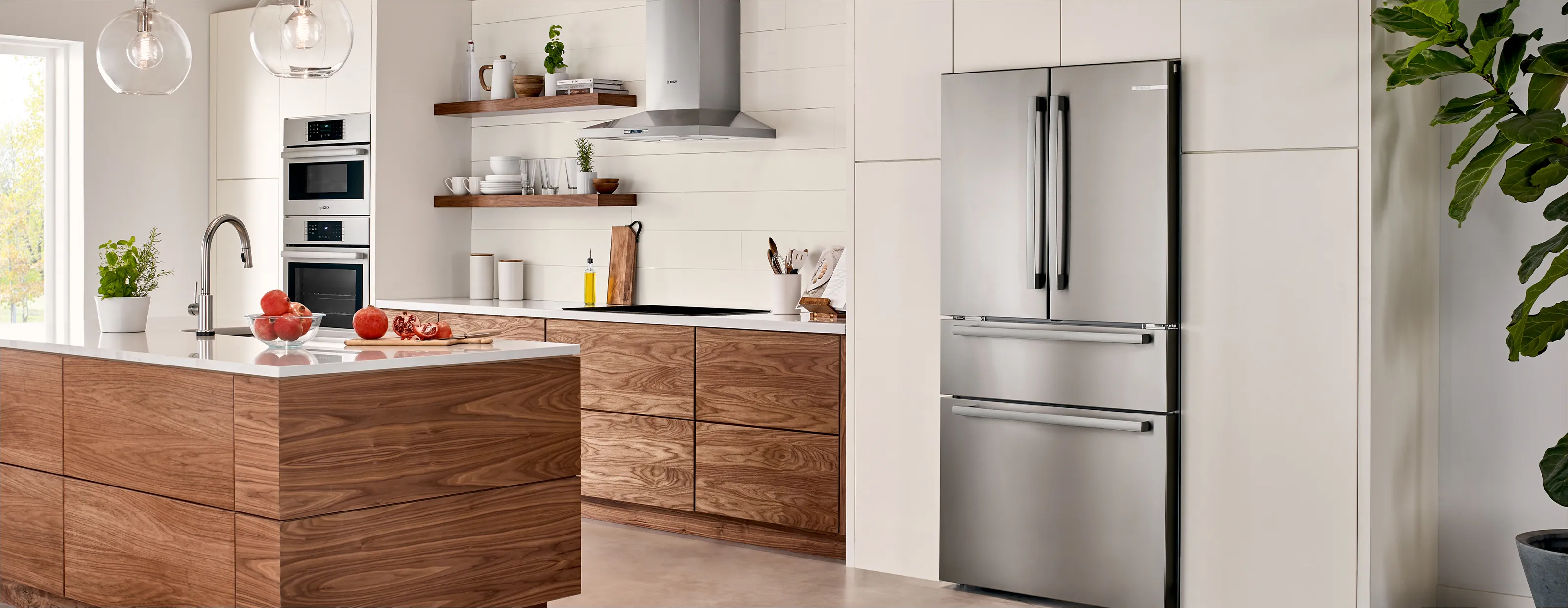 Modern kitchen with wood cabinets, white countertops, stainless steel appliances, open shelves, and hanging glass light fixtures.