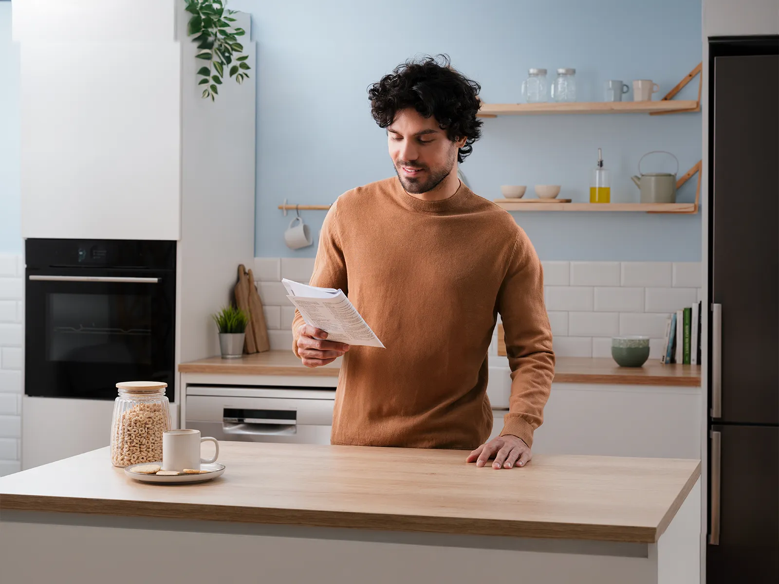 Ein Mann mit dunklen Locken steht in einer Küche und liest eine Anleitung. 