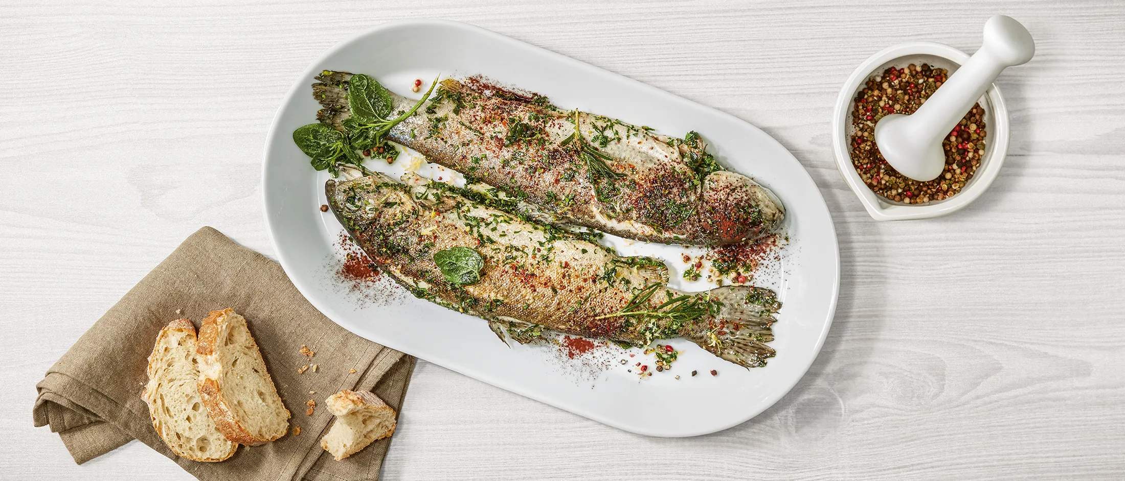 Grilled fish fillet with herbs, spices, and bread on a white plate.
