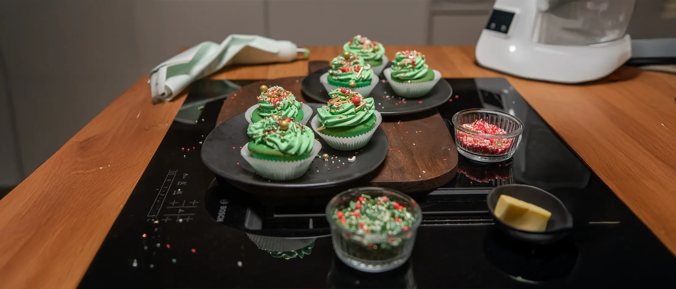 Child's hands holding a round cookie with green frosting and colorful sprinkles over a white plate.