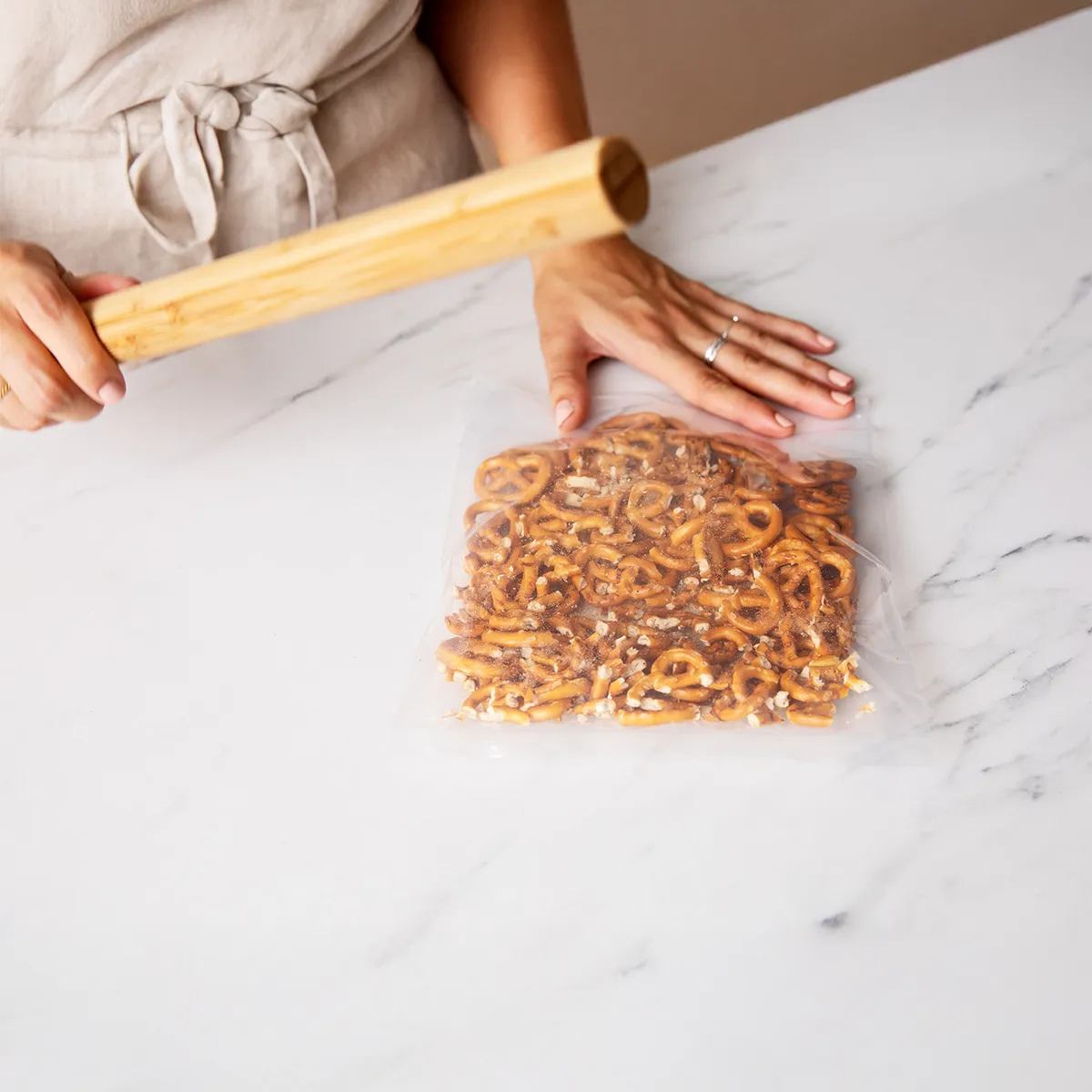 Hands spreading crushed pretzels and chocolate chunks over a baking sheet to make pretzel bark
