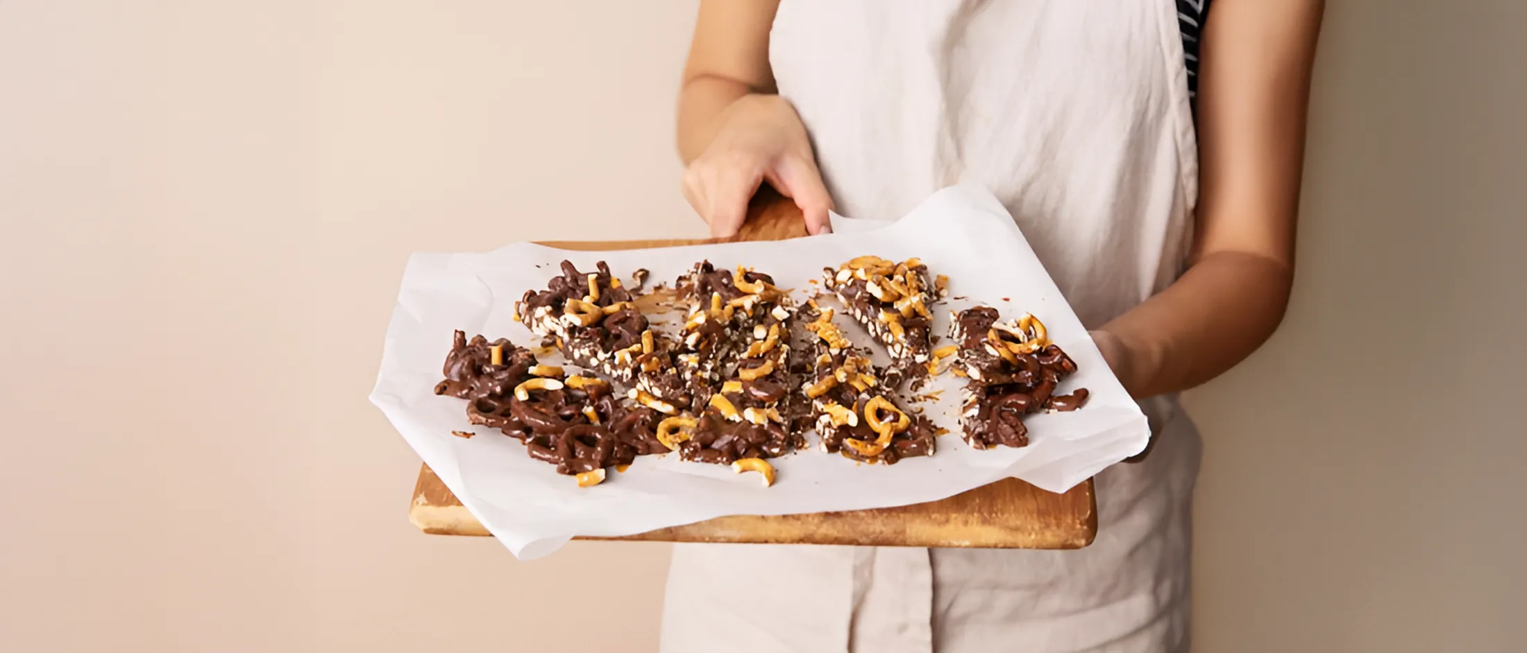 Hands spreading crushed pretzels and chocolate chunks over a baking sheet to make pretzel bark