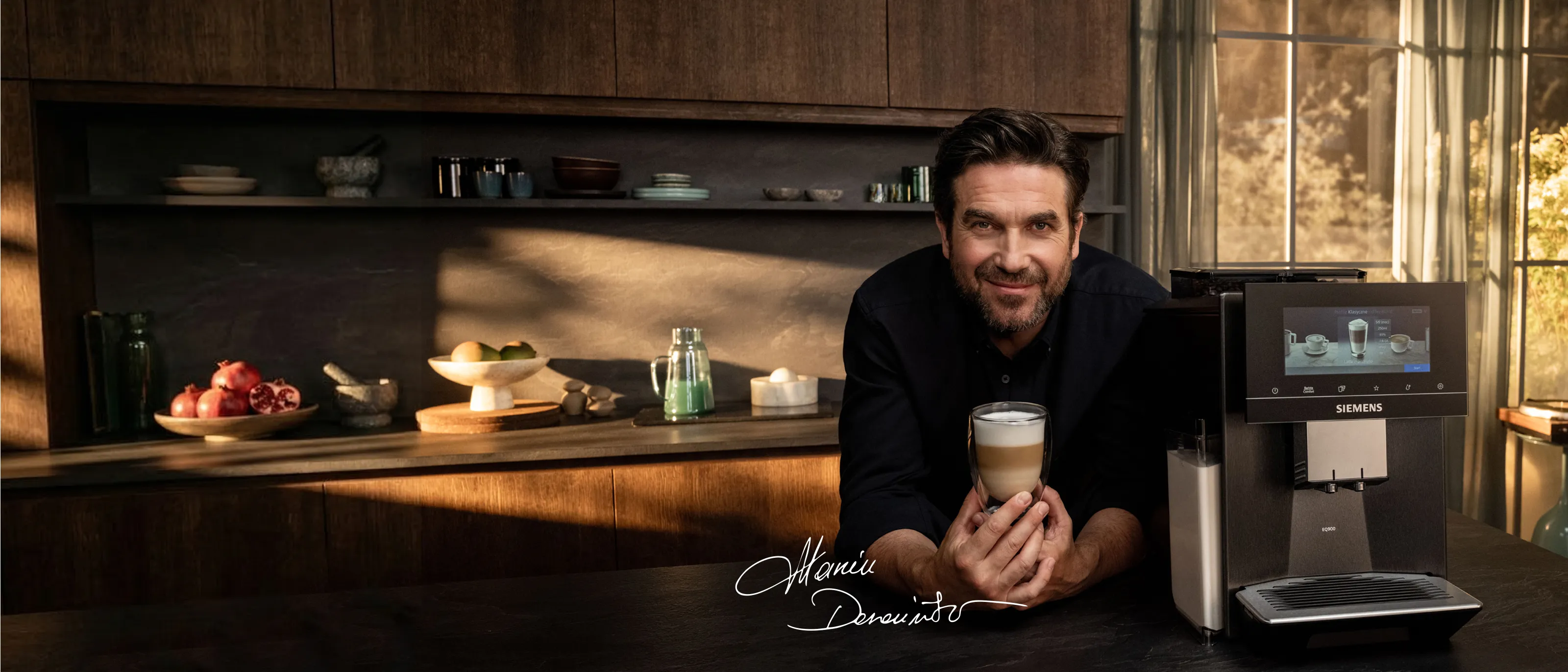 Mężczyzna trzymający filiżankę kawy obok ekspresu do kawy Siemens w eleganckiej  kuchni z dużymi oknami