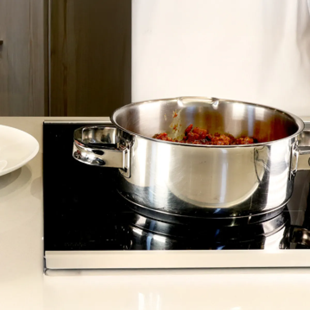 Stainless steel pot with red sauce cooking on a black stovetop in a modern kitchen.
