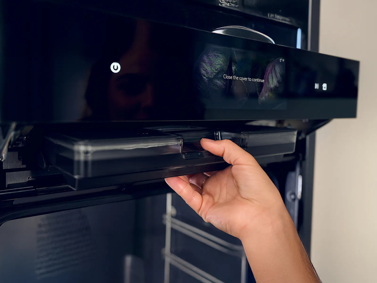 Hand removing or placing a tray inside a modern kitchen appliance with a digital screen displaying "Close the cover to continue."