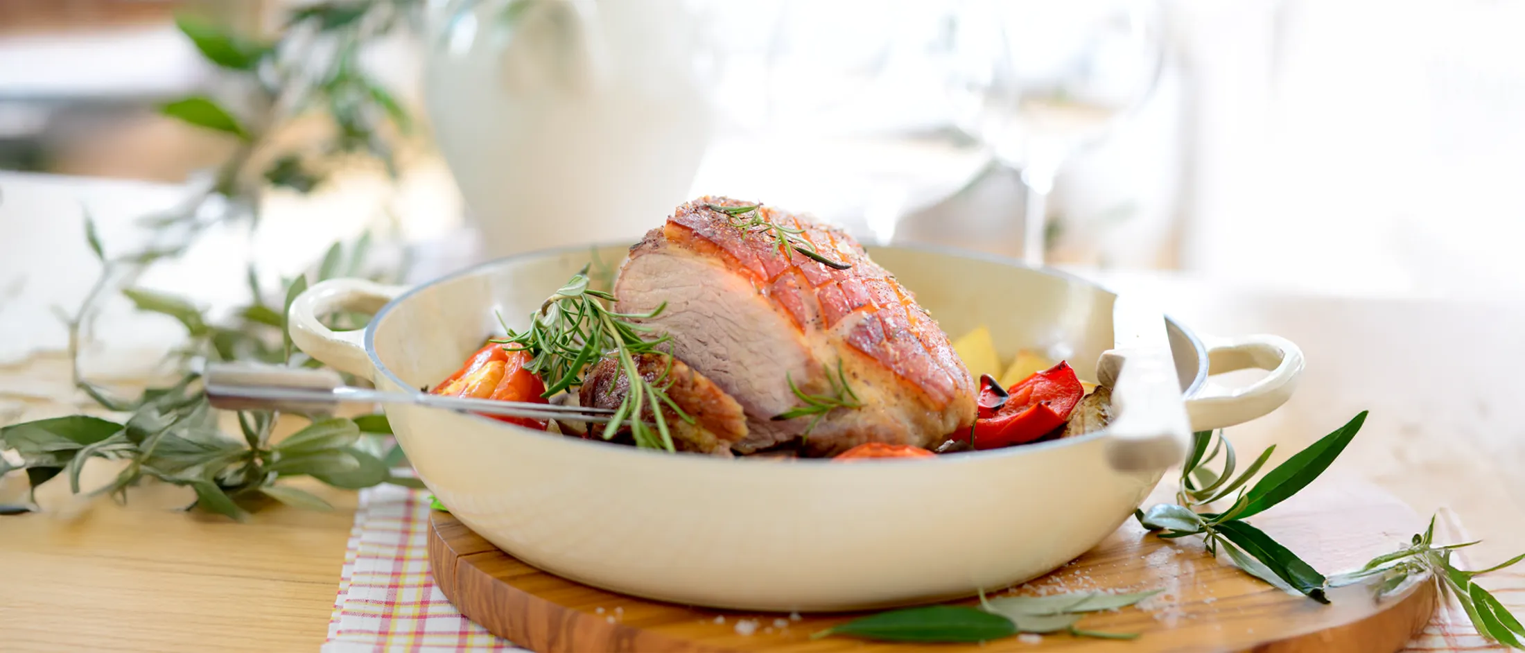 Roasted pork loin garnished with fresh rosemary and served with roasted vegetables in a white pan on a wooden board.